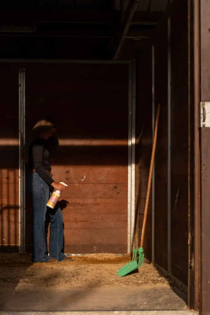 Horse owner in a stall at ground level, holding a bottle of Bye Bye Odor